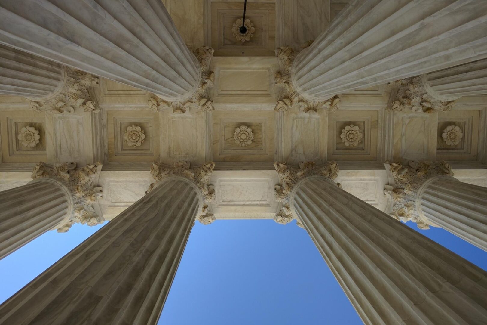 Upward view of large stone columns and ornate ceiling details against a clear blue sky.
