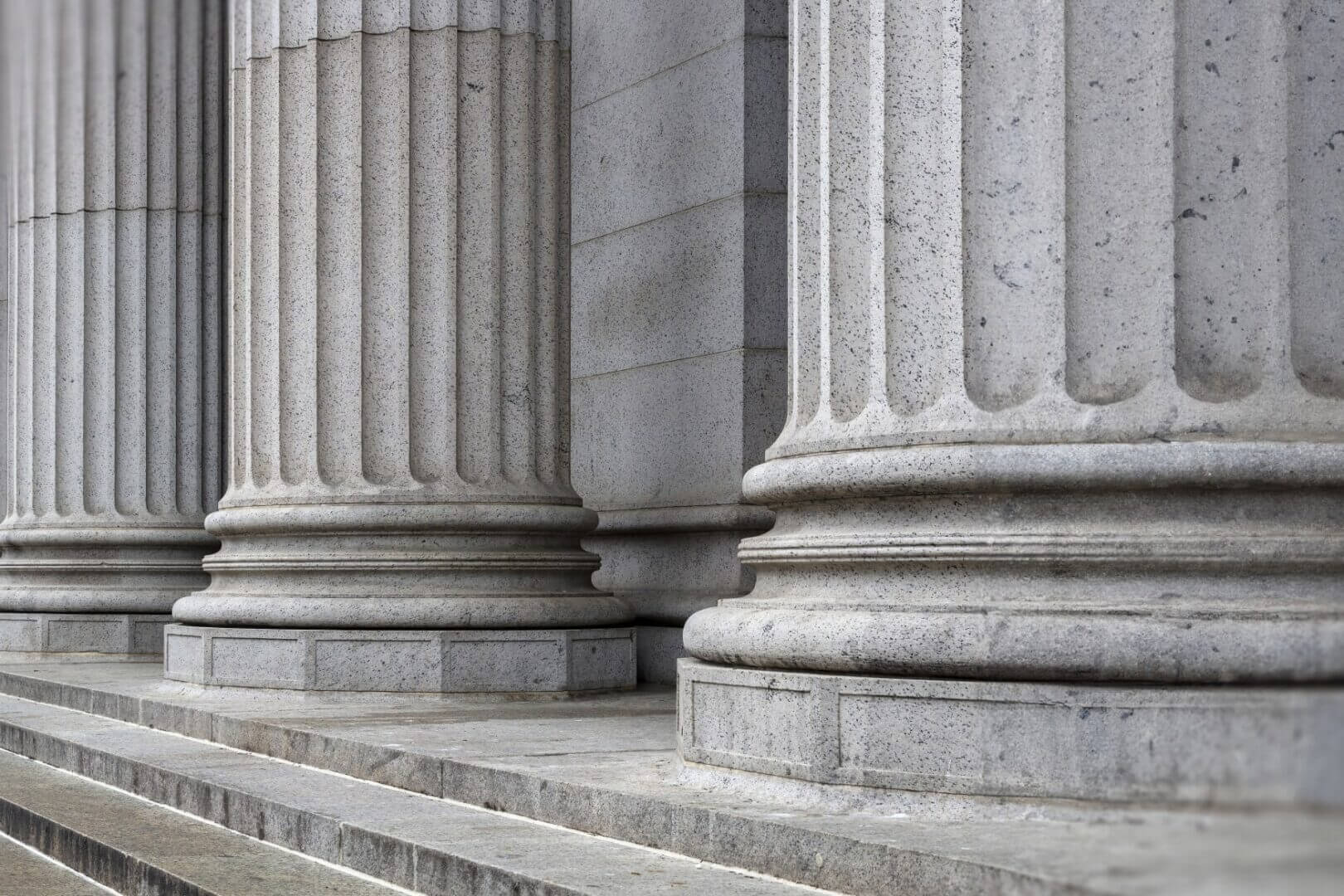 Close-up of large stone columns with fluted designs and square bases on a building.
